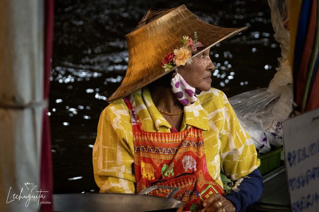 Lady with large hat preparing and selling delicious spicy food in her giant wok in Amphawa's floating markets, Thailand.