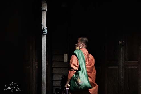 Monk hurrying across wooden homes near the temple in Amphawa, Thailand.