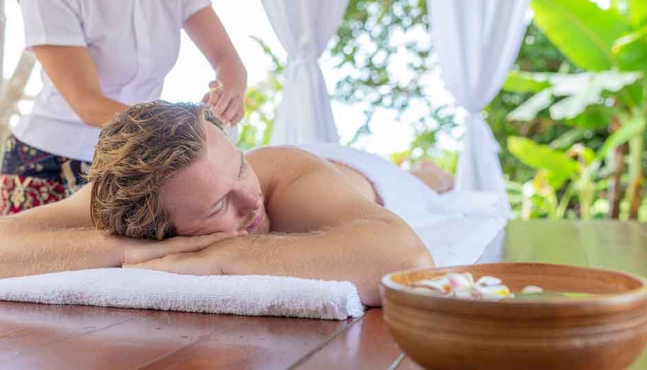 Man receiving a relaxing Balinese massage outdoors in a tropical spa setting.
