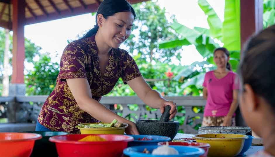 Balinese chef teaching participants how to prepare traditional dishes in an outdoor cooking class.