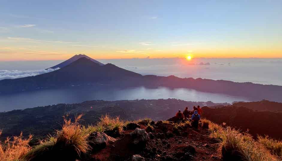 A group of trekkers on the summit of Mount Batur, looking out over the volcanic landscape at sunrise.