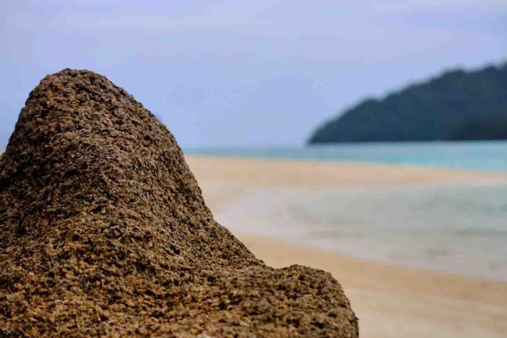 Close-up of a textured sand formation on a beach with a blurry background of turquoise water and a distant island in Phuket.